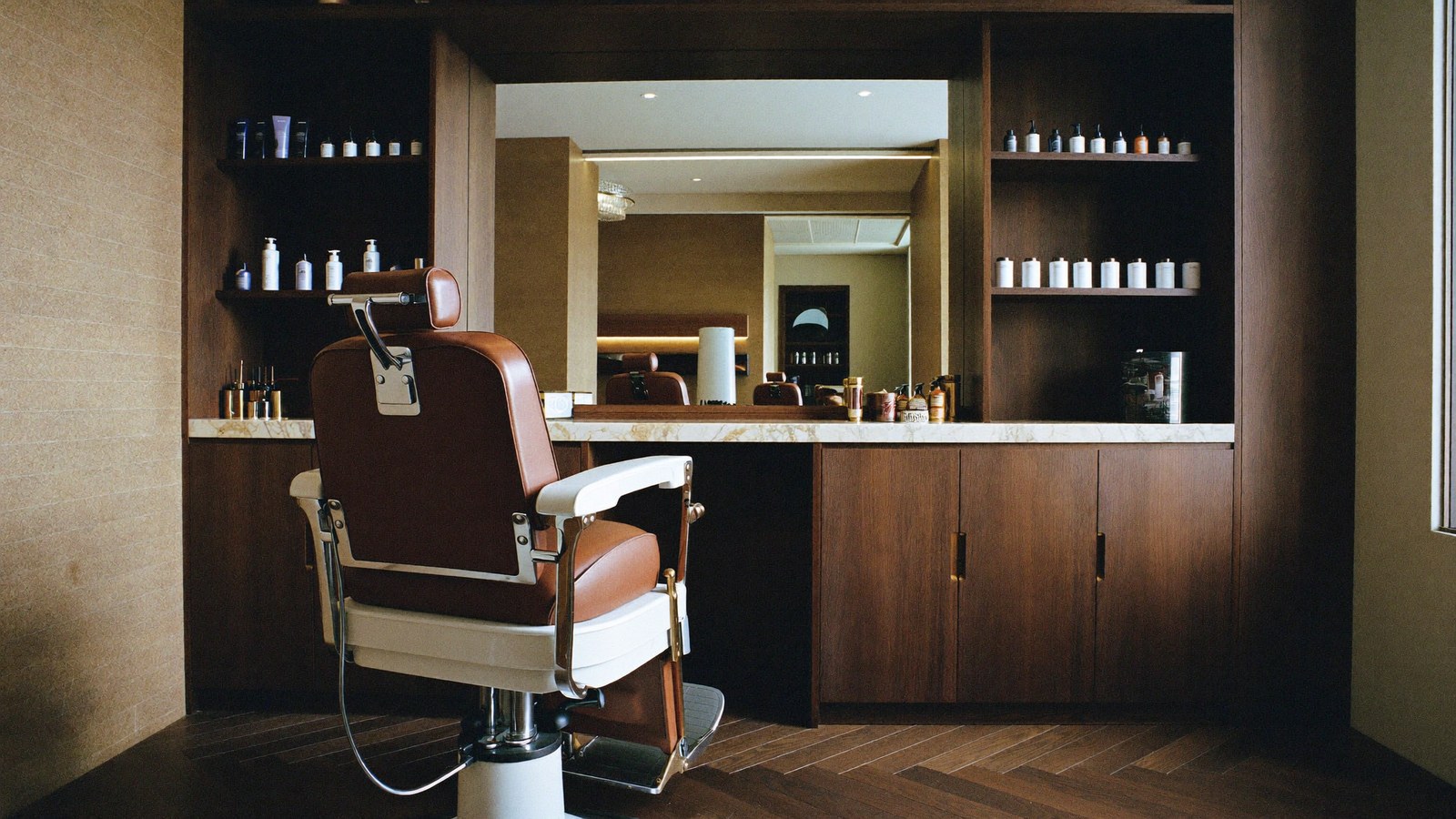 Intérieur haut de gamme de salon de barbier : fauteuil en cuir, parquet chevron, comptoir en marbre et miroir — concept de site qartz.dev