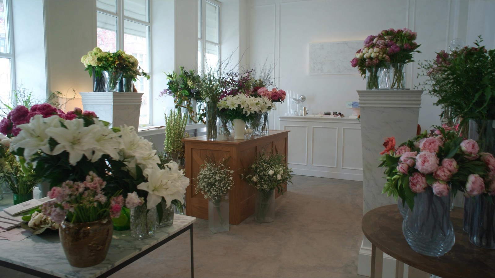 Boutique de fleuriste élégante et lumineuse : bouquets de pivoines dans des vases sur comptoirs en marbre — concept de site fleuriste qartz.dev