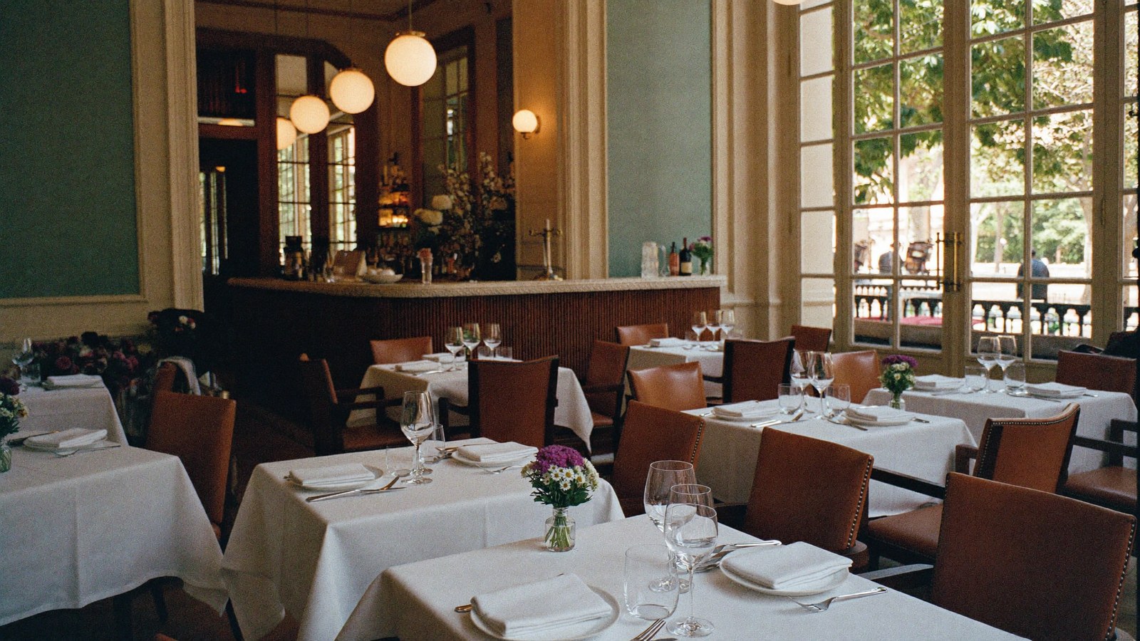 Salle de restaurant élégante : tables nappées de blanc, chaises en cuir, baies vitrées et bar — concept de site restaurant qartz.dev
